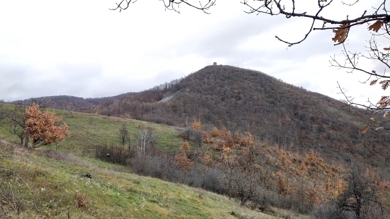 Obronci Radan planine sa livadama i ogoljenom šumom, a na vrhu brda mala kamena kula