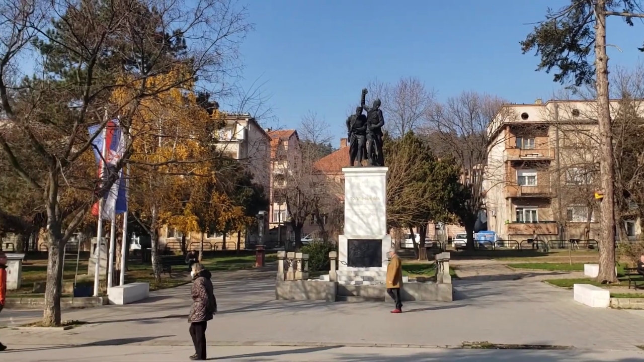 Spomenik palim Topličanima u gradskom parku sa ljudima u prolazu i zgradama u pozadini